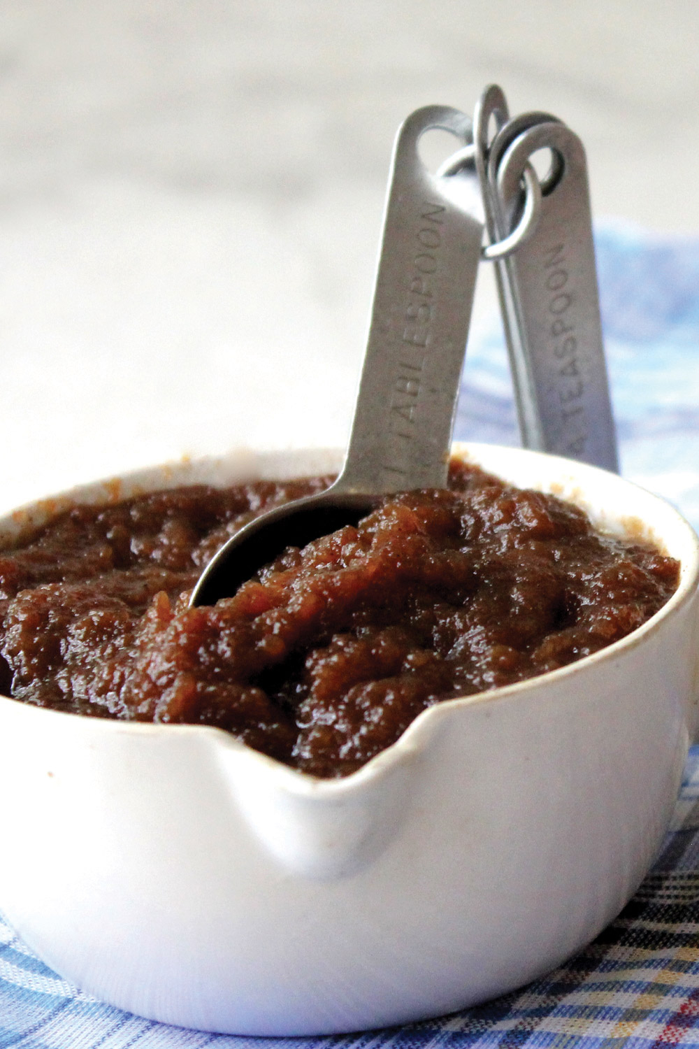 Measuring cup full of apple butter with measuring spoon standing in the thick brown apple butter
