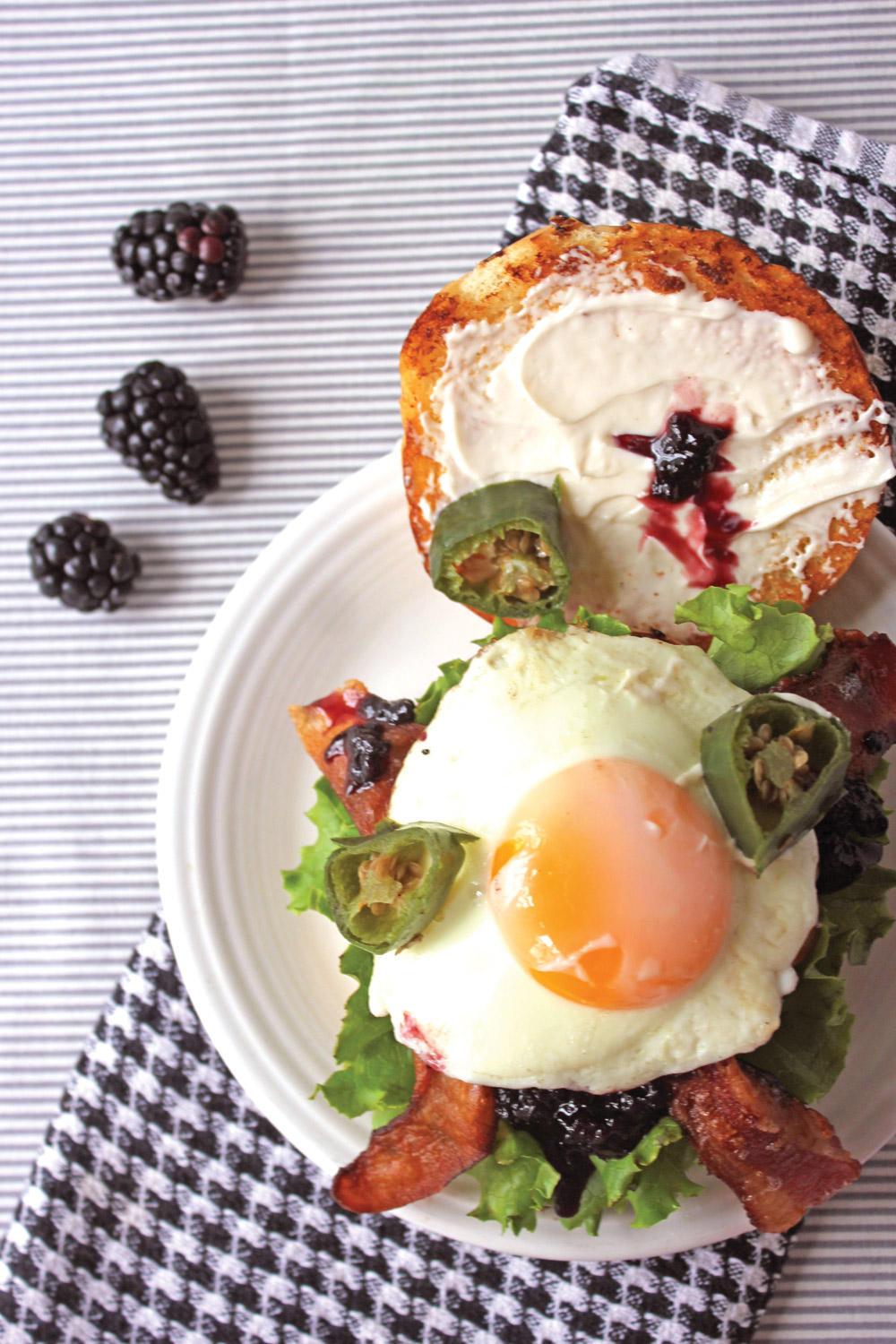 Overhead view of burger with sunny side up egg, ackberry jam, jalepenos, and lettuce with blackberries on side