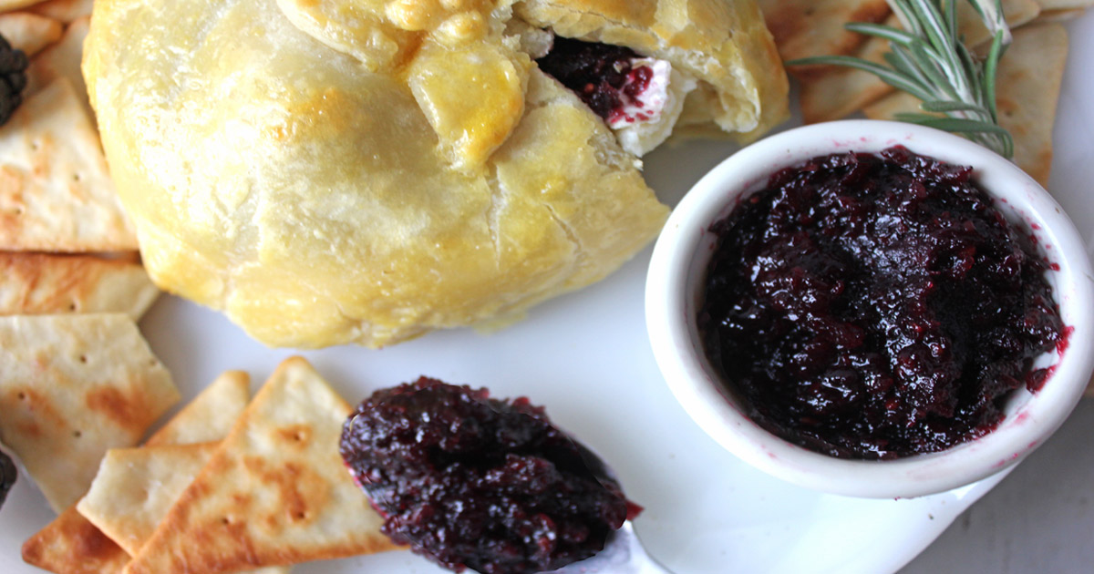 Baked brie in puff pastry with blackberry jam and on appetizer plate.