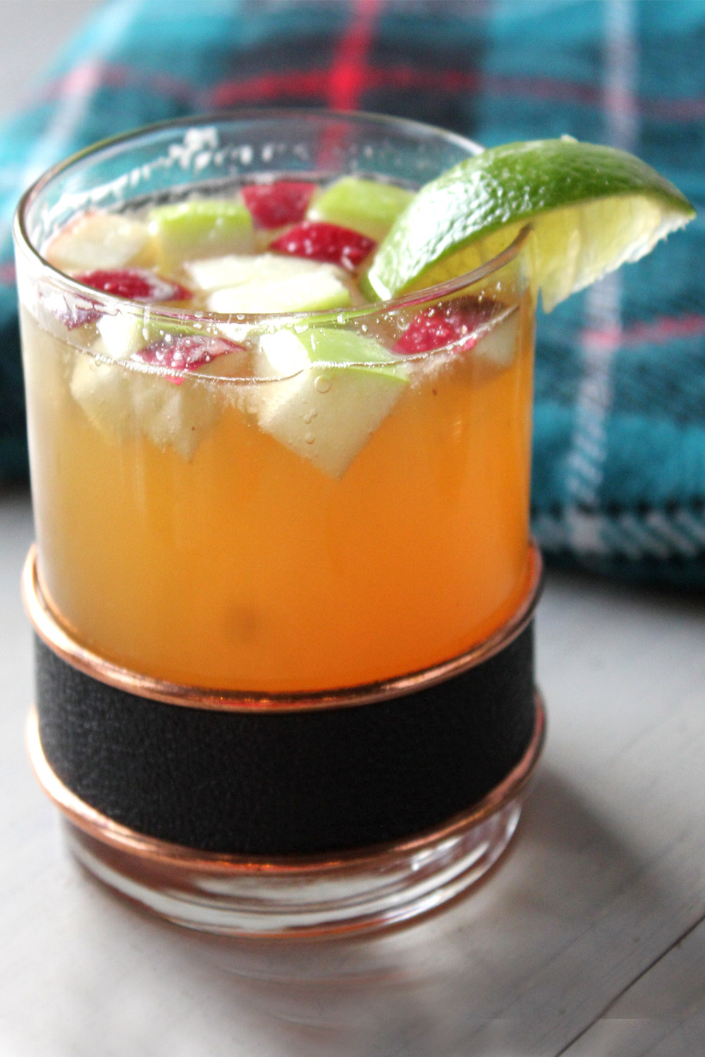 Bourbon and apple cider cocktail topped with red and green cubed apples and lime wedge