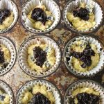 Shows blueberry muffins in tin, half full with blueberry jam spoooned in.