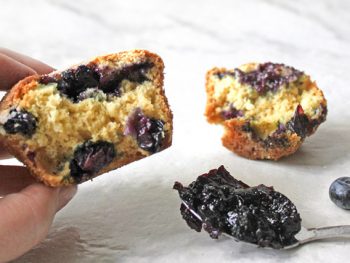 Hand holding half blueberry muffin revealing blueberry jam center with blueberries