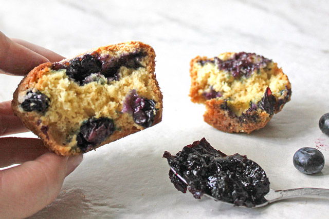 Hand holding half blueberry muffin revealing blueberry jam center with blueberries