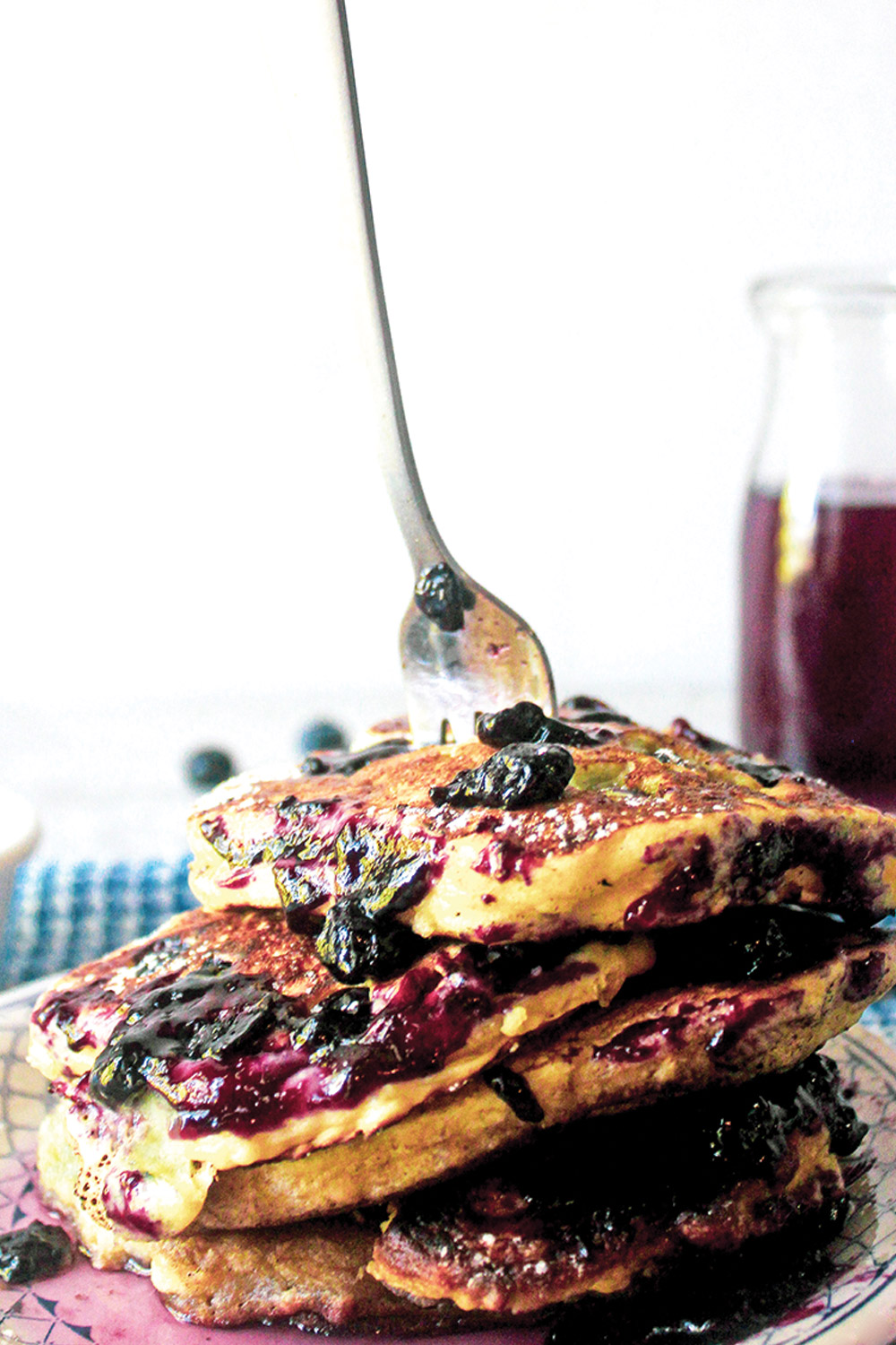 Blueberry pancake stack dripping with blueberries and jam syrup with a fork stuck upright in the top