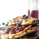 Casual stack of blueberry pancakes with a blueberry jam syrup bottle in background
