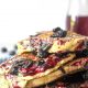 Staggered stack of blueberry pancakes with blueberries and blueberry jam syrup dripping down sides
