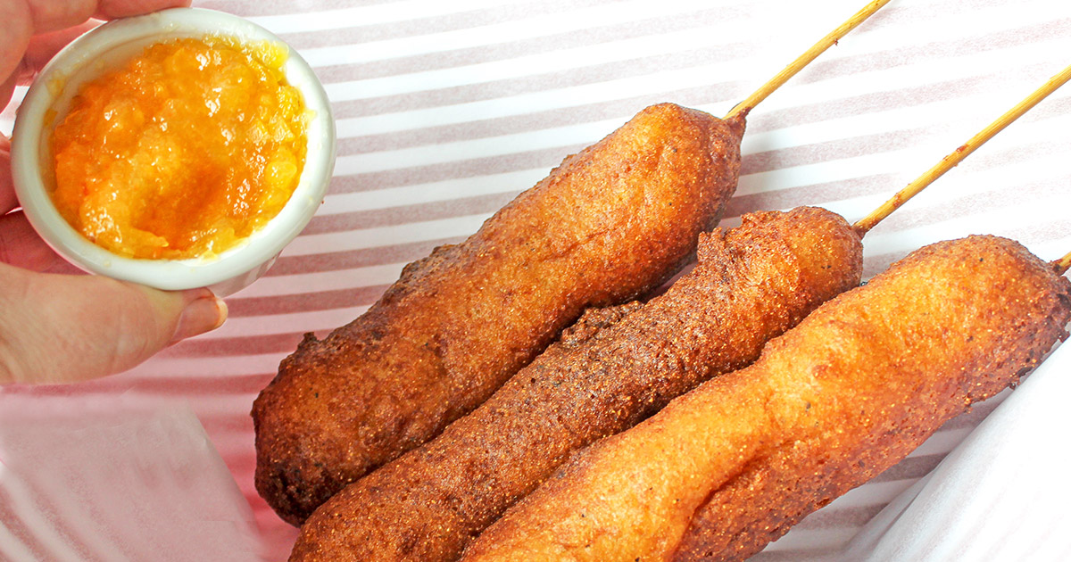 Three homemade corn dogs in lined serving basket with peach habanero jam dipping bowl