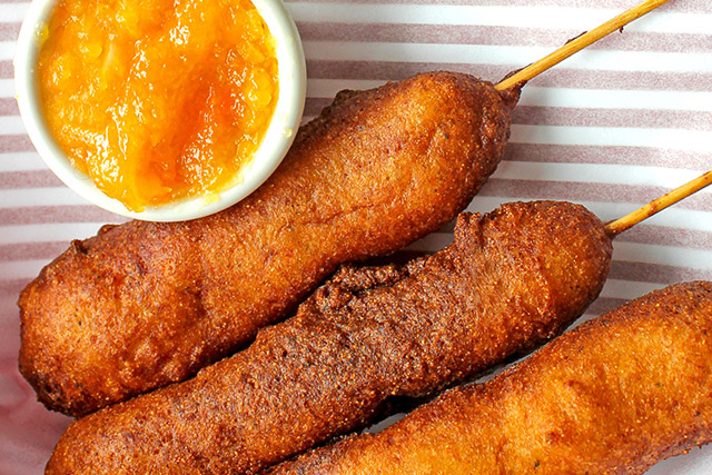 Tight shot of corn dogs in a basket with peach habanero jam in a side dish