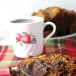 Slice of apple bread slathered with apple butter on a red and green placemat with cup of coffee and more slices of bread in background