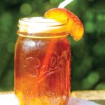 Cocktail of sweet tea peach jam and bourbon in mason jar with straw