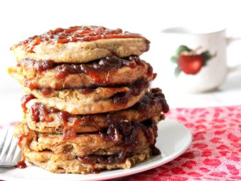 Tall stack of spiced apple butter pancakes oozing apple butter between layers and in a spiral swirl on top layer with an apple coffee cup in background