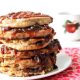 Tall stack of spiced apple butter pancakes oozing apple butter between layers and in a spiral swirl on top layer with an apple coffee cup in background