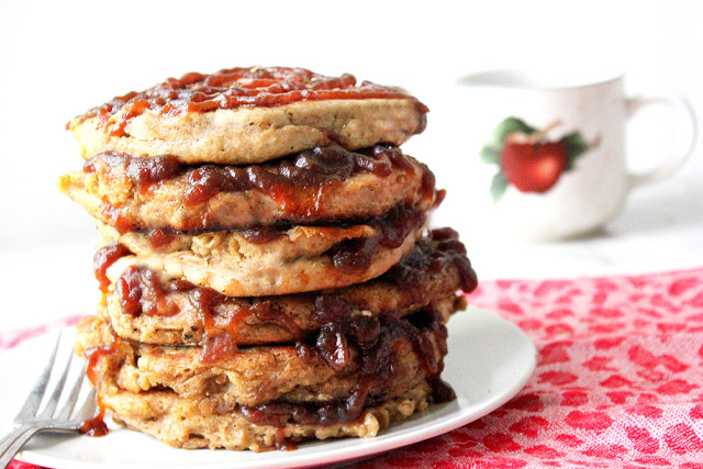 Tall stack of spiced apple butter pancakes oozing apple butter between layers and in a spiral swirl on top layer with an apple coffee cup in background