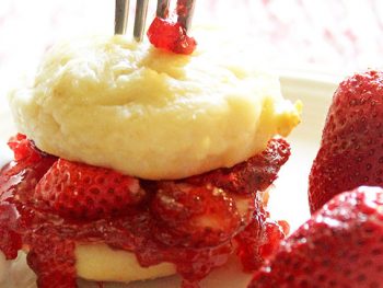 Strawberry shortcake scones layered with strawberry jam and fresh strawberries with a fork sticking straight up in the top