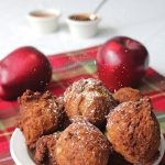 Bowl of round apple butter fritters showered with powdered sugar