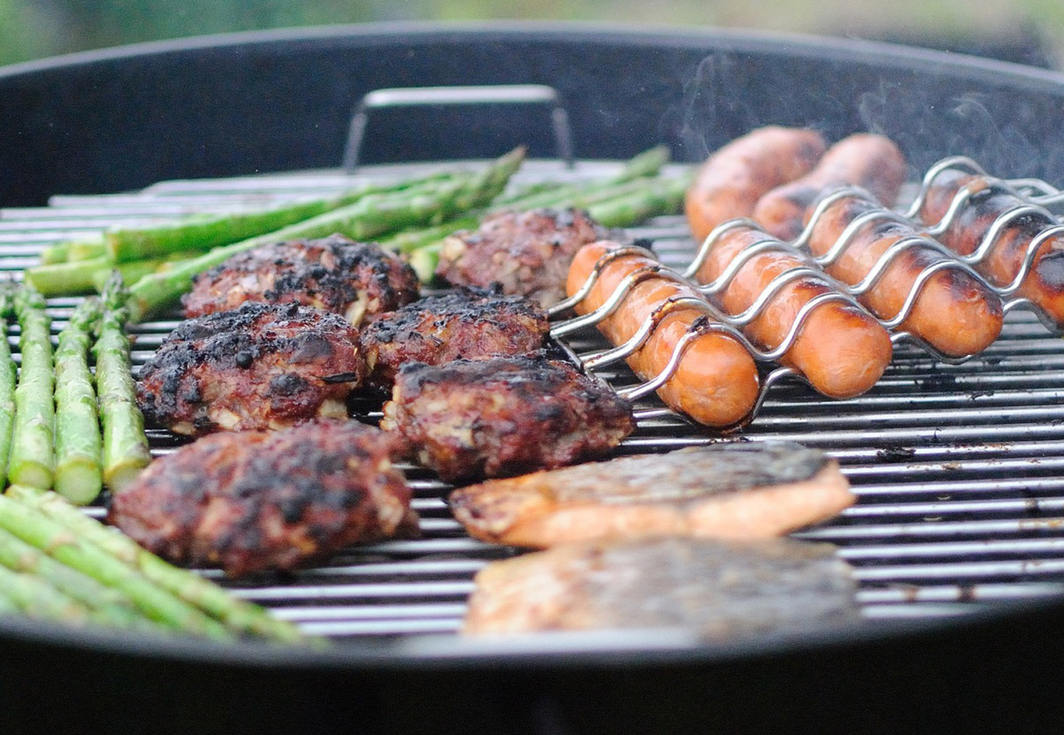 Backyard BBQ with charcoal grill loaded with hamburgers and hot dogs