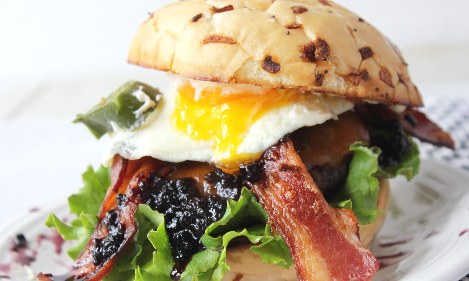 Burger with egg on a onion bun with bacon, peppers, and blackberry jam