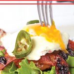 Fork diving into a fried egg, topping a blackberry jam and jalepeno bacon cheeseburger