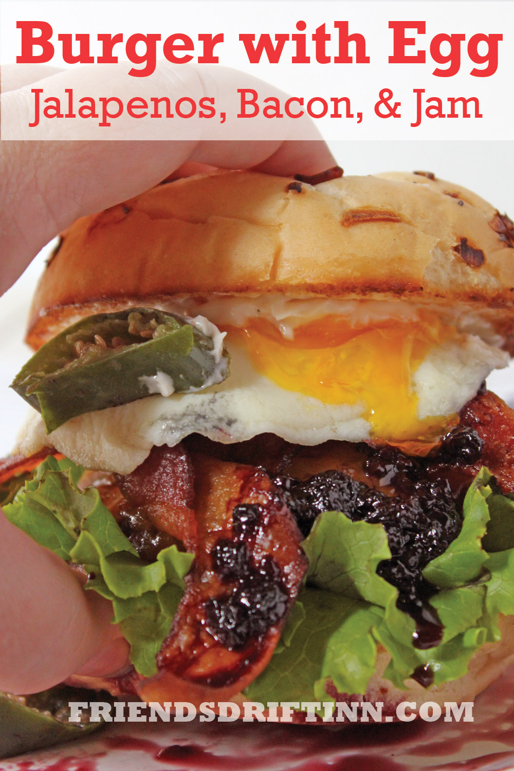 Hand holding a huge burger with egg, bacon, jalapenos and blackberry jam