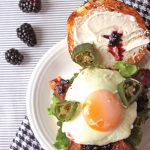 Overhead view of open burger with sunny side up egg, blackberry jam and jalapeno peppers