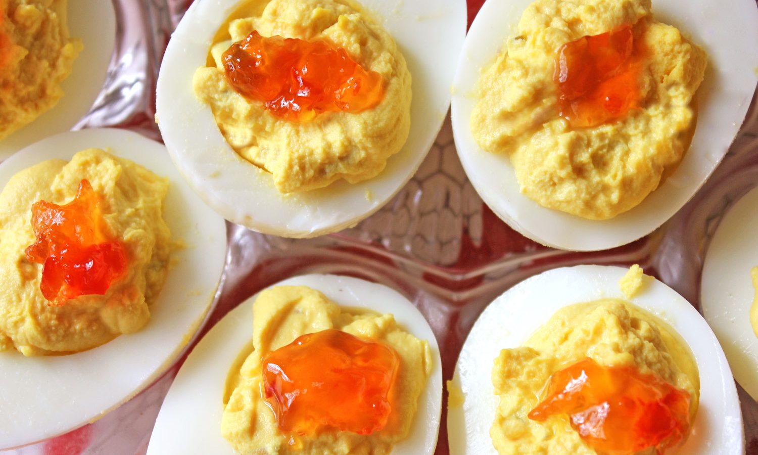 Plated deviled eggs with red pepper jelly garnish