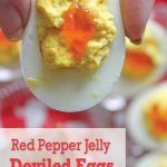Red Pepper Jelly garnish on deviled egg with hand above deviled egg platter