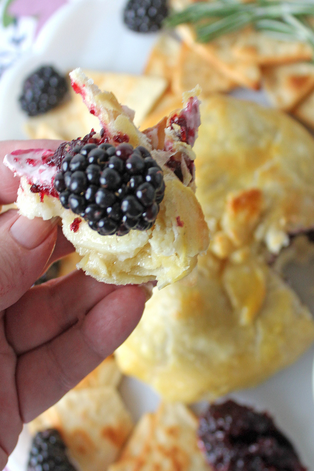 Hand holding chunk of baked brie with berries and jam.