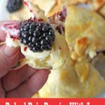 Hand with a bite of baked brie with fresh blackberries and blackberry jam.