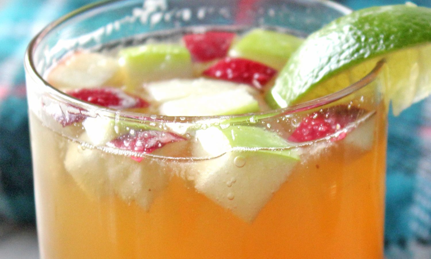 Tight shot of apple cubes and lime wedge floating on bourbon apple cider cocktail