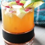 Rocks glass with bourbon apple cider over ice, topped with festive cubes of green and red apples.